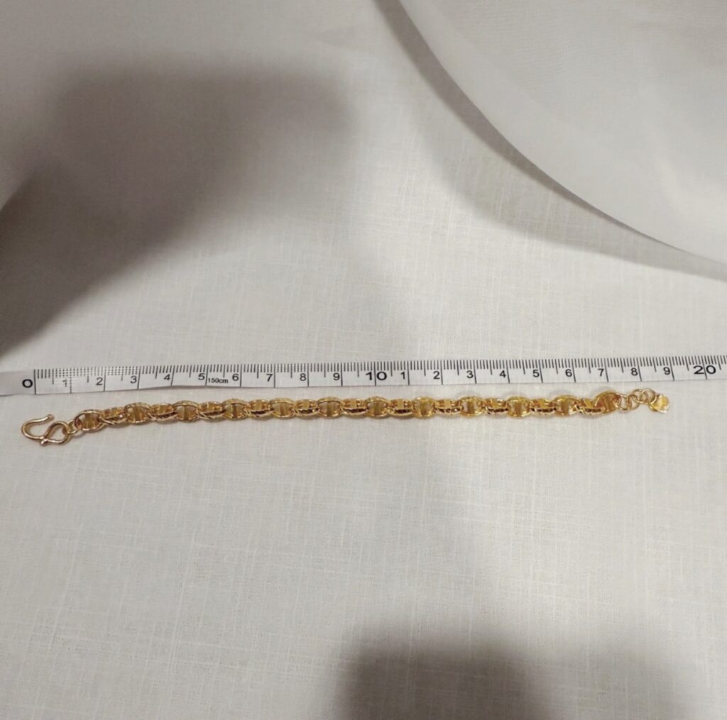 將金色鏈條手鍊平放，用捲尺測量手鍊長度的示範。