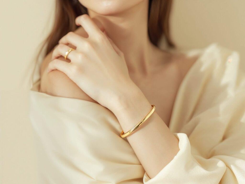 女生優雅佩戴黃金手鍊與戒指，手部線條柔美，金飾在溫暖光線中展現細緻光澤。